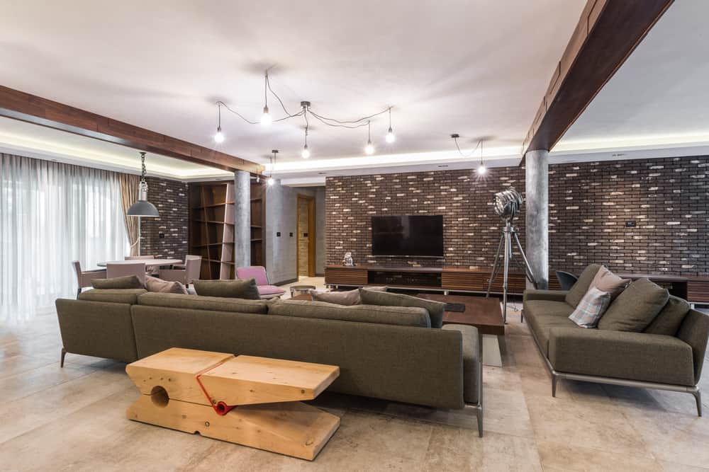 Modern living room with green sofas, a brown wooden coffee table, TV on a brick wall, and pendant lighting