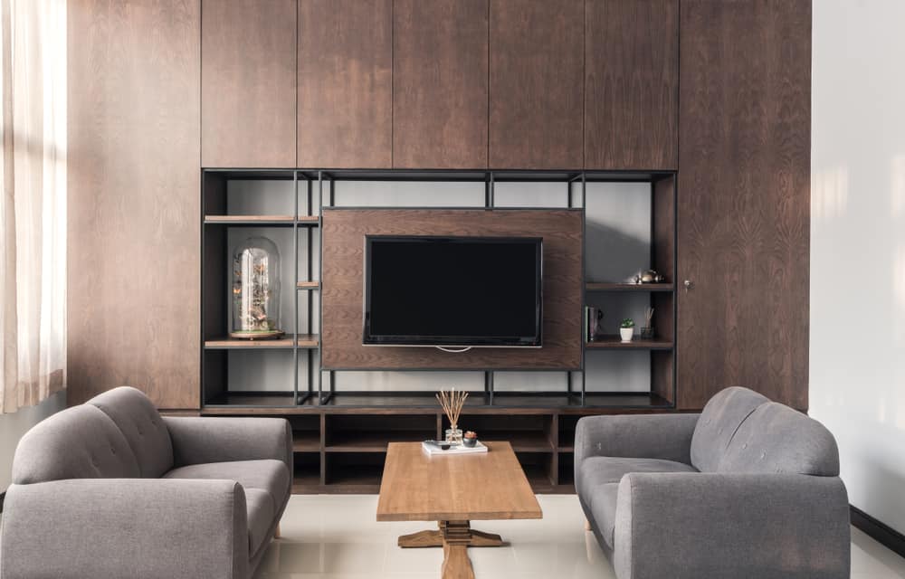 Modern living room with a brown wood wall, TV, two gray sofas, and a wooden coffee table