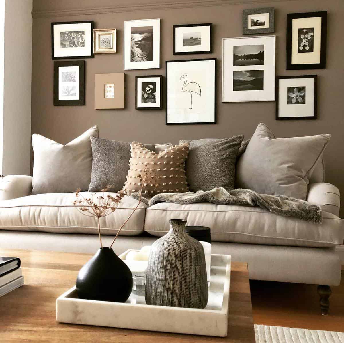 Cozy living room with a beige sofa, gray pillows, and a brown gallery wall featuring decor that includes a tray with vases