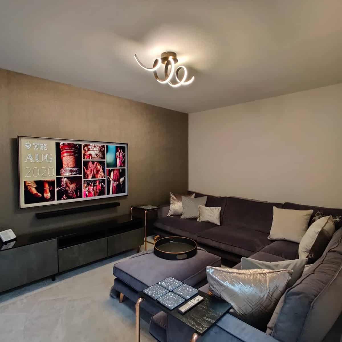 Modern living room with a large TV, gray sectional sofa, brown decorative pillows, and a unique ceiling light