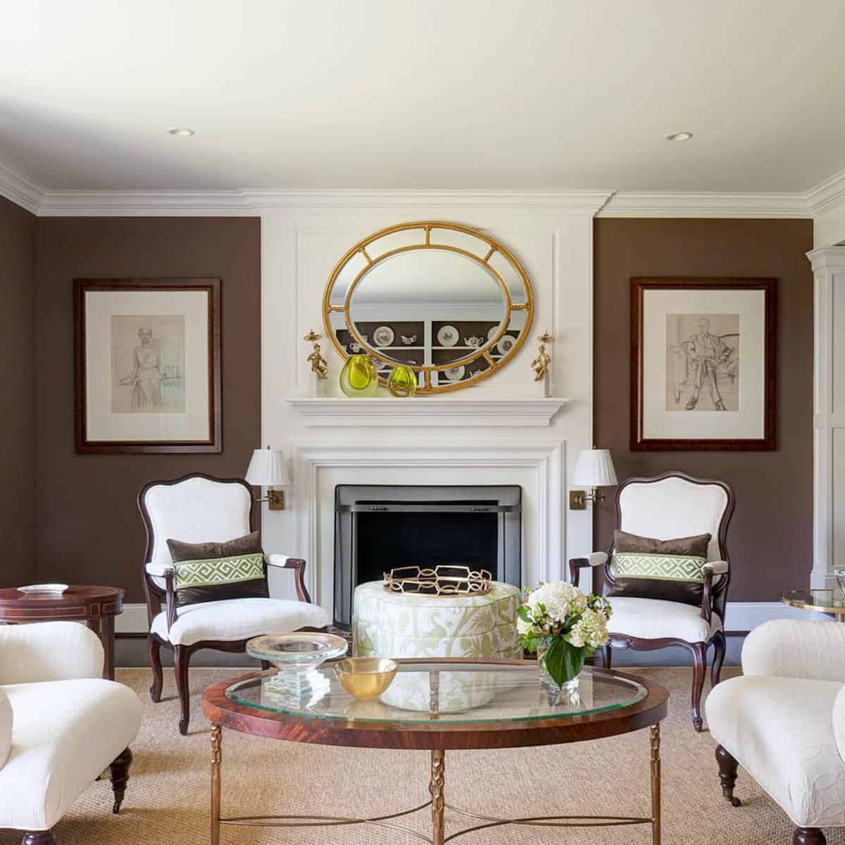 Elegant living room with brown armchairs, a glass coffee table, a round mirror, and framed art beside the fireplace