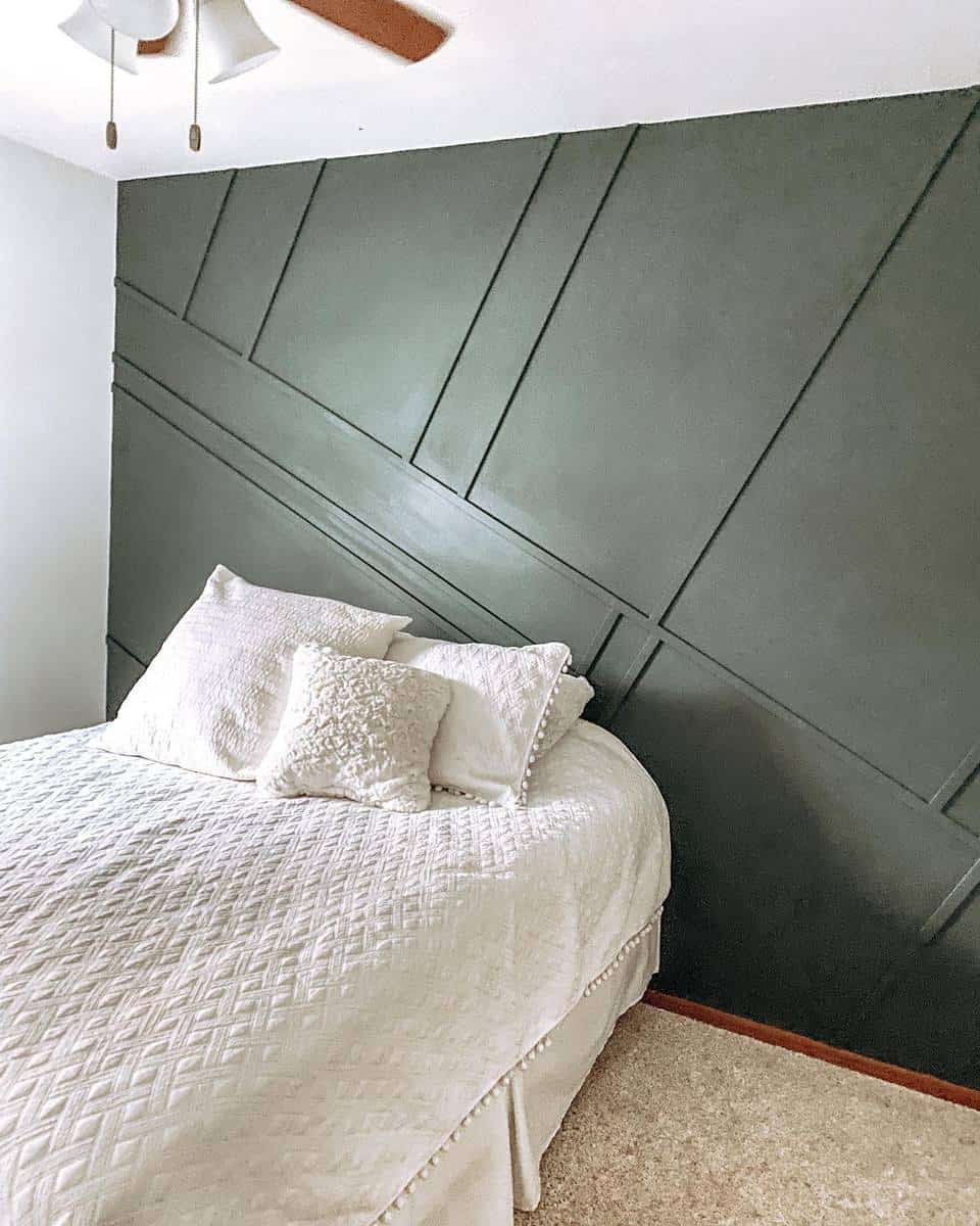 Cozy bedroom with a white bedspread and pillows, set against a dark green geometric accent wall