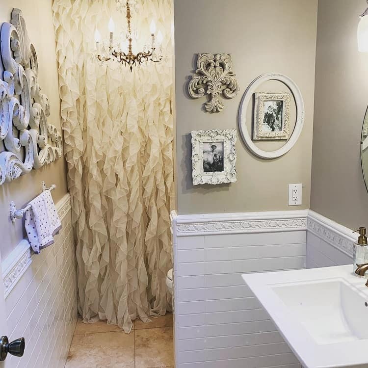 Farmhouse bathroom with decorative frames, a ruffled shower curtain, and a chandelier above tiled walls and sink