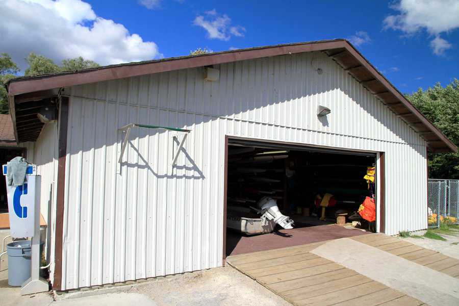 Large white aluminum shed with an open garage door, housing equipment and tools inside.