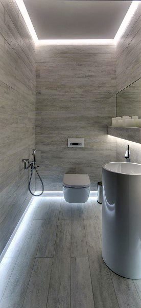 Modern bathroom with wood panels, wall-mounted toilet, pedestal sink, and accent lighting near the floor