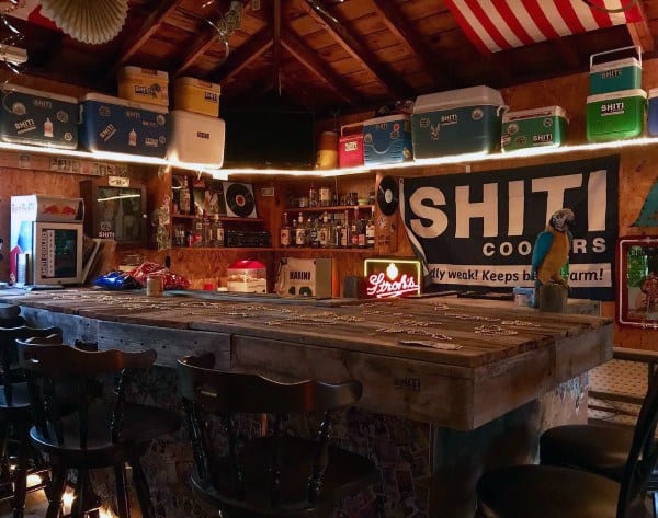 Rustic garage bar with wooden decor, stools, neon lights, and Shiti Coolers branding.