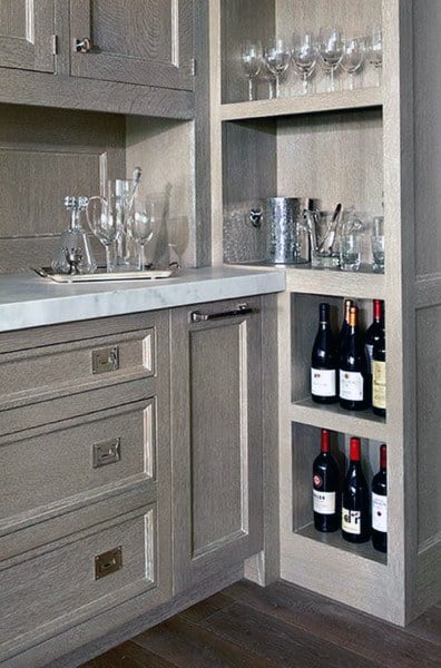 Compact home bar with wine storage, glassware, and marble countertop in gray cabinetry.