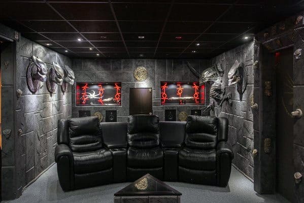 Home theater with black leather recliners in a sci-fi themed room, featuring alien sculptures and red neon lights