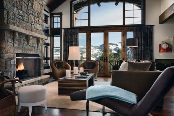 Cozy living room with a fireplace, modern furniture, and large windows overlooking a snowy mountain landscape