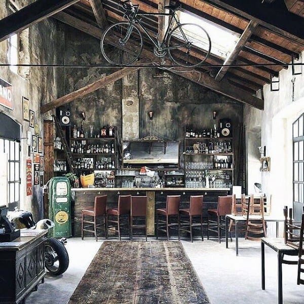 Vintage garage bar with rustic shelves, bar stools, hanging bike, and industrial decor.