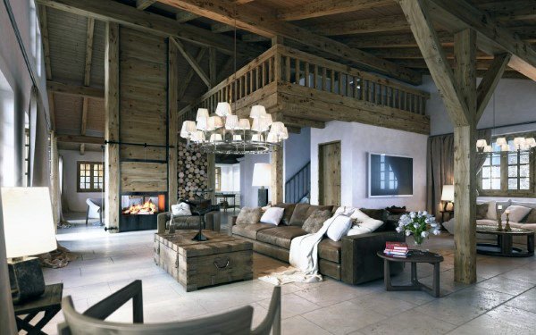 Rustic living room with wooden beams, a cozy fireplace, and a large sofa; stacked firewood and chandeliers add charm