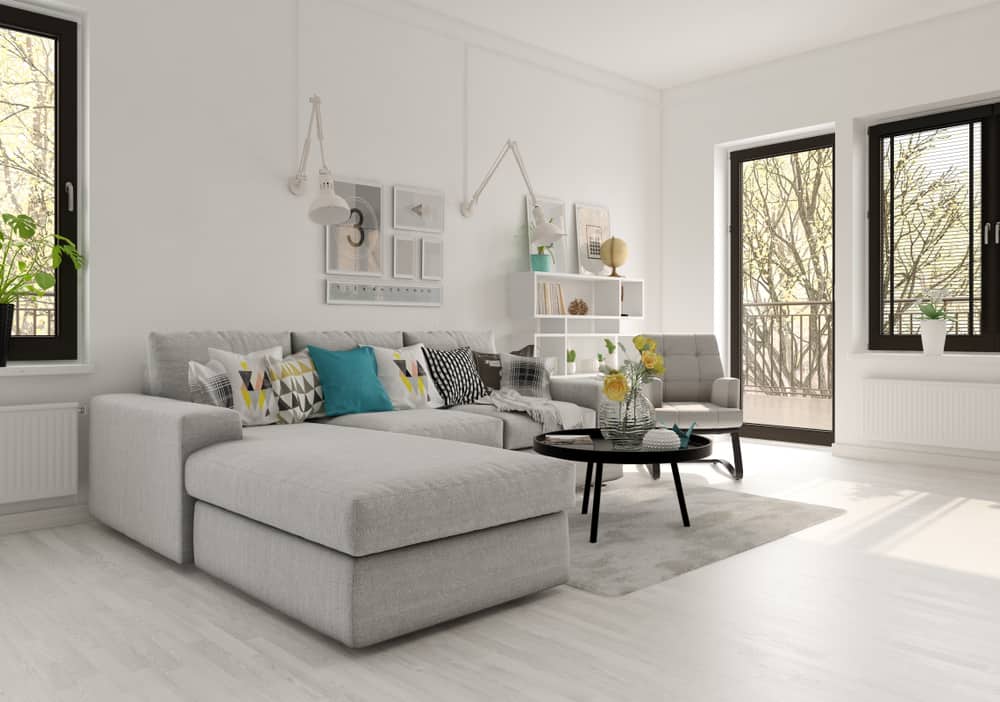 Modern living room with a gray sectional sofa, colorful cushions, black coffee table, and natural light from large windows