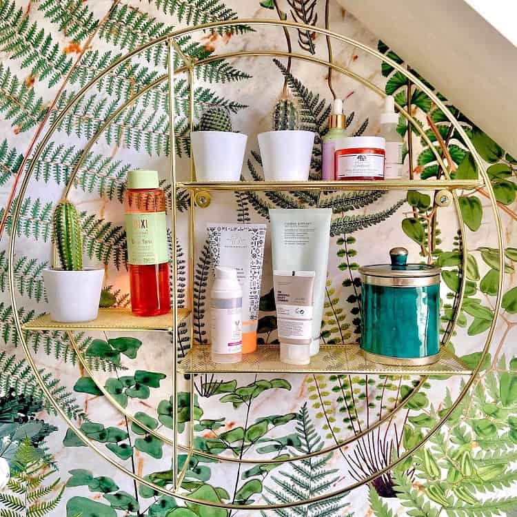 Bathroom with fern mural wallpaper and gold circular shelf holding plants and skincare items.