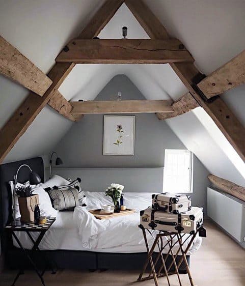 Cozy attic bedroom with exposed wooden beams, a neatly made bed, and suitcases on a stand