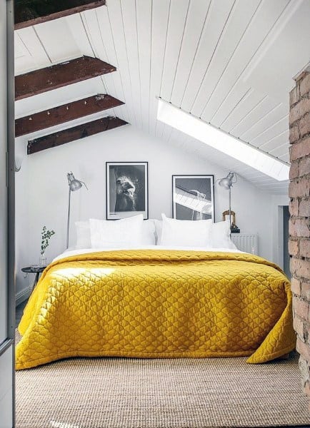 Cozy attic bedroom featuring a yellow quilt, white walls, skylights, and two black-and-white framed photos