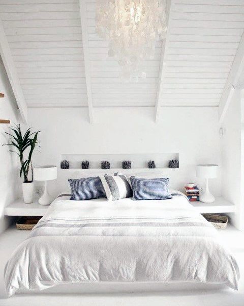 Minimalist bedroom with a pitched white ceiling, featuring a bed with blue pillows and a hanging pendant light