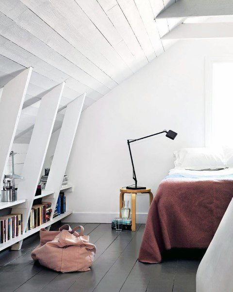 White attic bedroom with built-in bookshelf, angled ceiling, and cozy bedding.