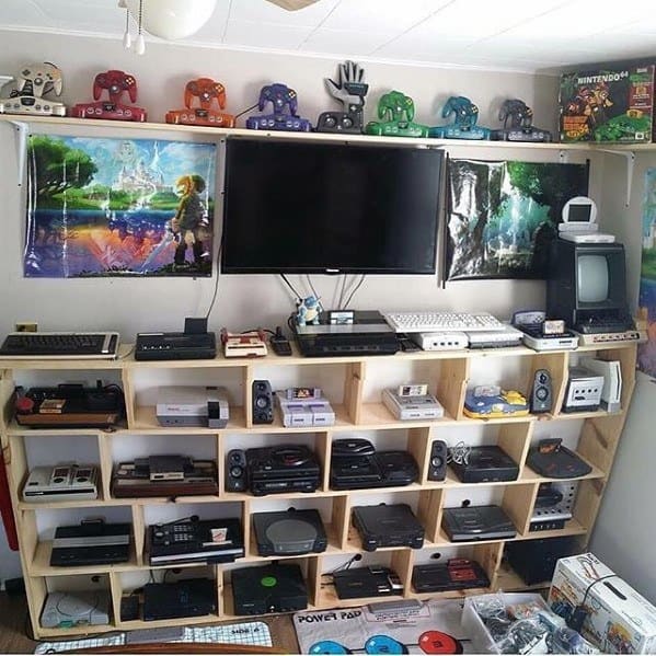 A room with shelves displaying retro gaming consoles, controllers, and posters on the walls