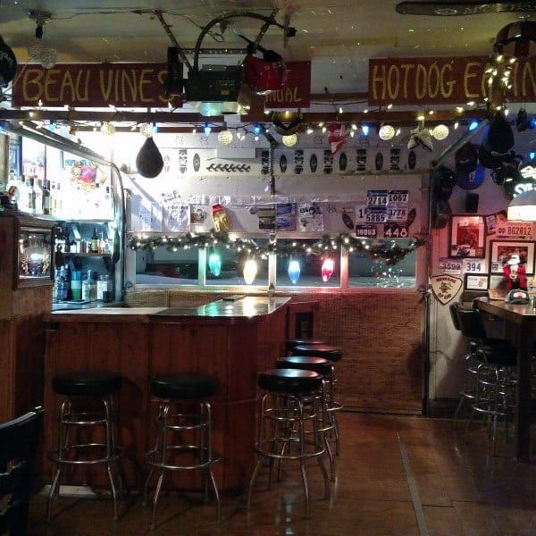 Eclectic garage bar with wooden counter, string lights, vintage signs, and bar stools.