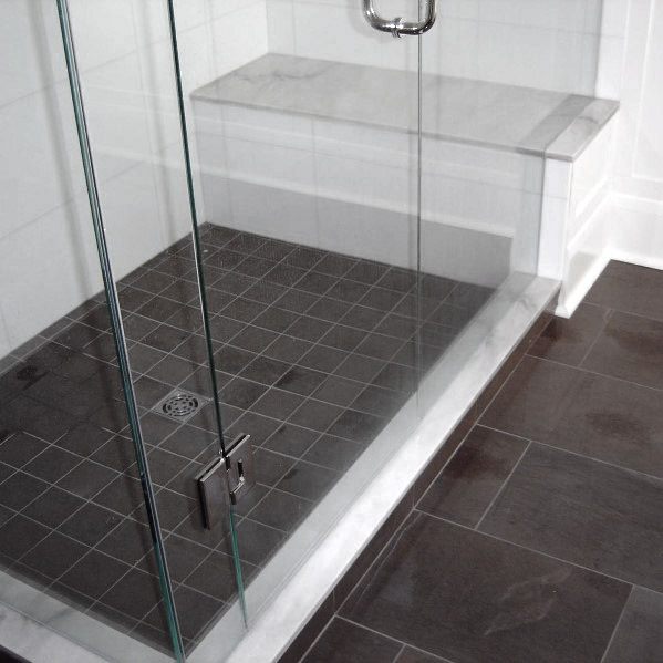 Grey glass shower door with a tiled floor and built-in shower bench