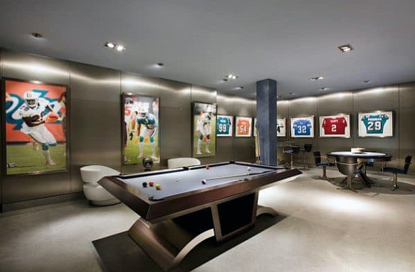 Modern sports-themed mancave with sleek pool table, framed jerseys, player murals, and lounge chairs.