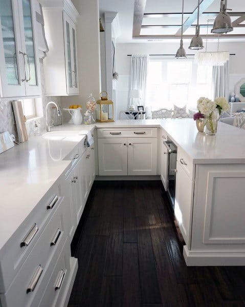 Bright white kitchen with dark hardwood flooring, white cabinetry, and elegant countertops