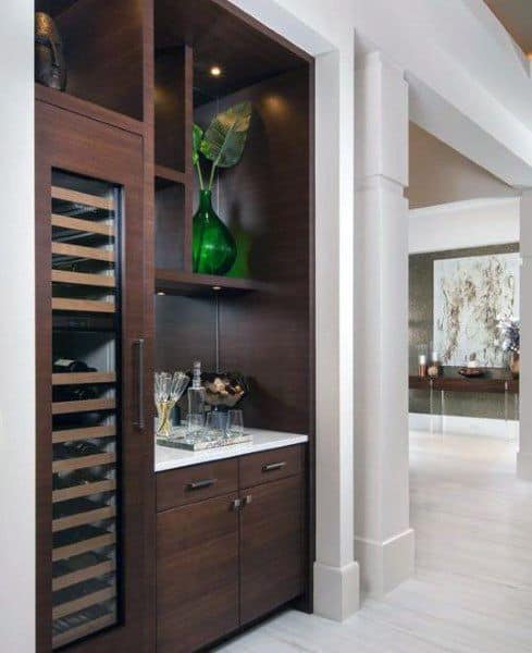 Modern mini bar with wine fridge, dark wood cabinets, white countertop, and green decor accents.