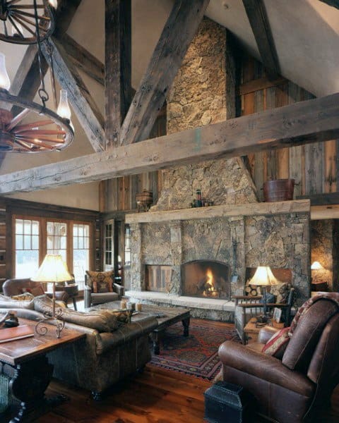 A rustic living room with a towering stone fireplace, wooden beams, and warm, inviting furniture, creating a cozy atmosphere