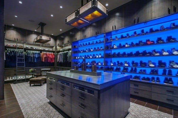 A luxurious walk-in closet with blue-lit shelves displaying clothes and shoes, centered by a sleek island