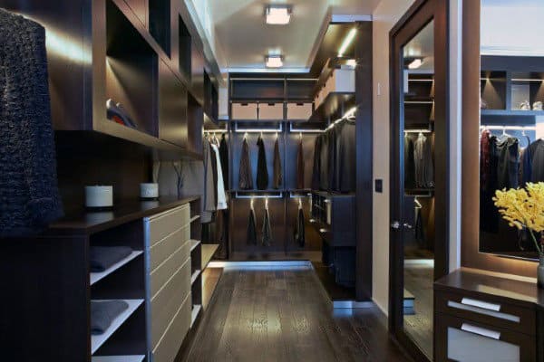 Modern walk-in closet with dark wood shelves, hanging clothes, and a full-length mirror