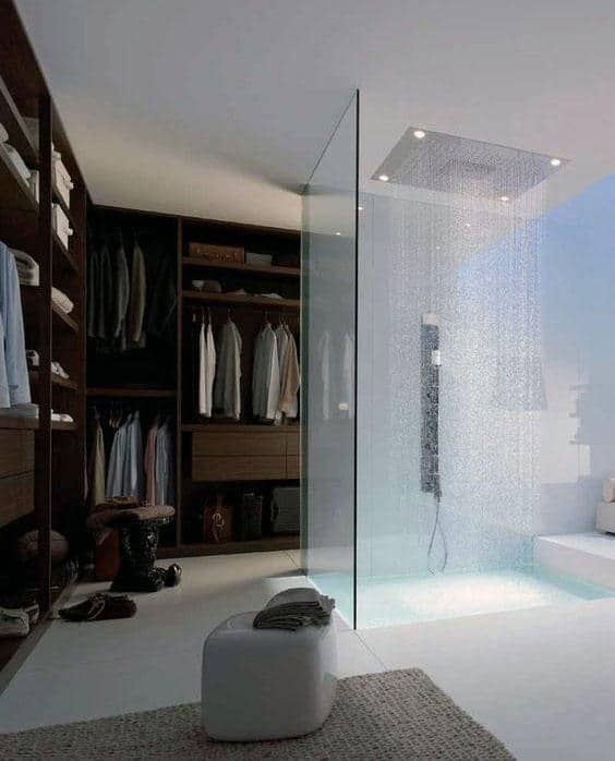 Modern bathroom with a glass shower, open wardrobe, and neatly arranged clothes on shelves and hangers