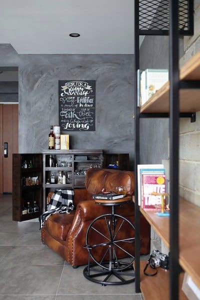 Industrial mini bar with dark shelving, leather armchair, chalkboard art, and rustic decor.