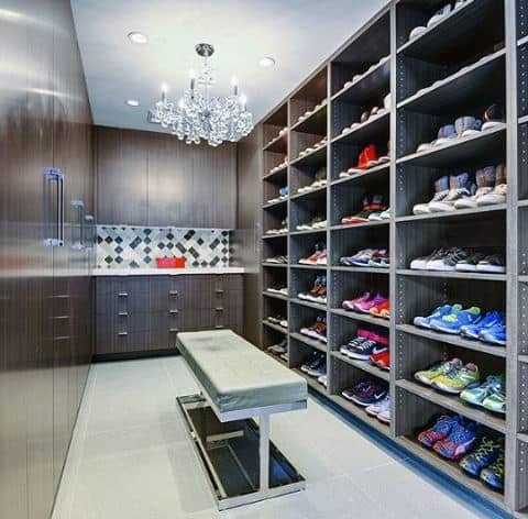 Spacious shoe closet with shelves filled with sneakers and a bench in the center under a chandelier