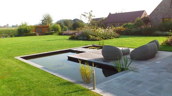 Contemporary tiled pond with a wooden deck, featuring stylish seating and surrounded by a lush lawn.