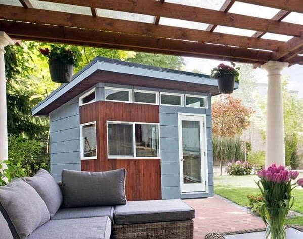 Modern backyard shed with a slanted roof, large windows, and a cozy patio.