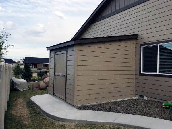 Small beige shed with a slanted roof attached to the side of a house in a suburban yard.