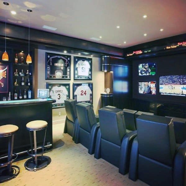 Modern mancave interior with sleek black bar, leather theater seats, and framed sports jerseys.