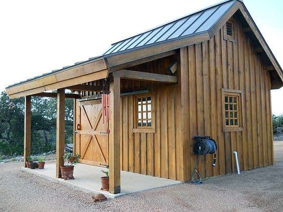 Rustic wooden shed with a metal slanted roof, barn door, and covered porch in a rural area.