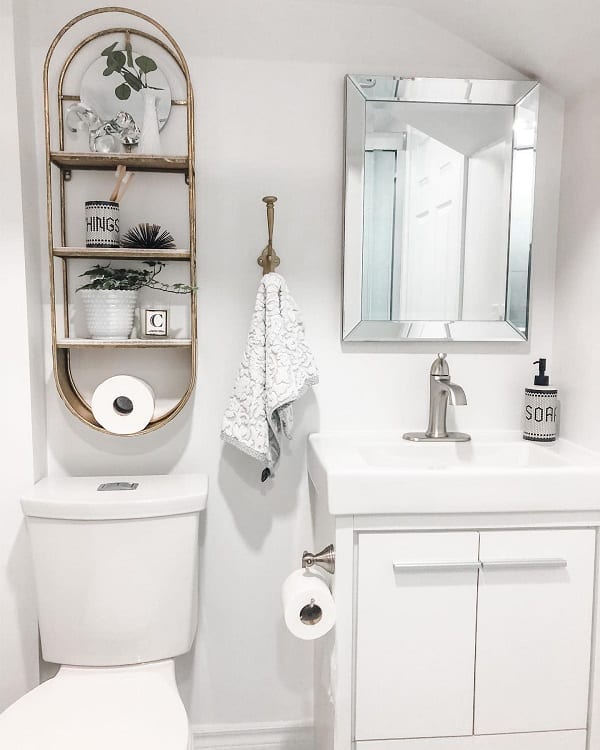 Modern white bathroom with gold shelving, plants, and minimalistic decor above toilet.