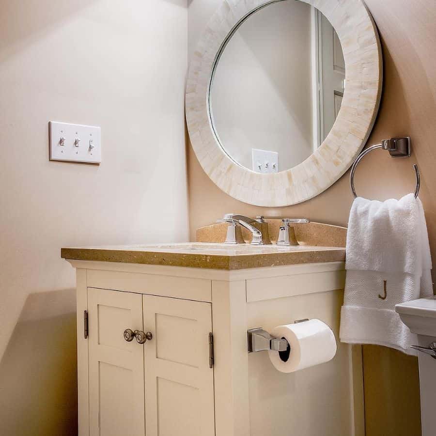 Bathroom with a round mirror, beige vanity, and towel on a metal ring holder.