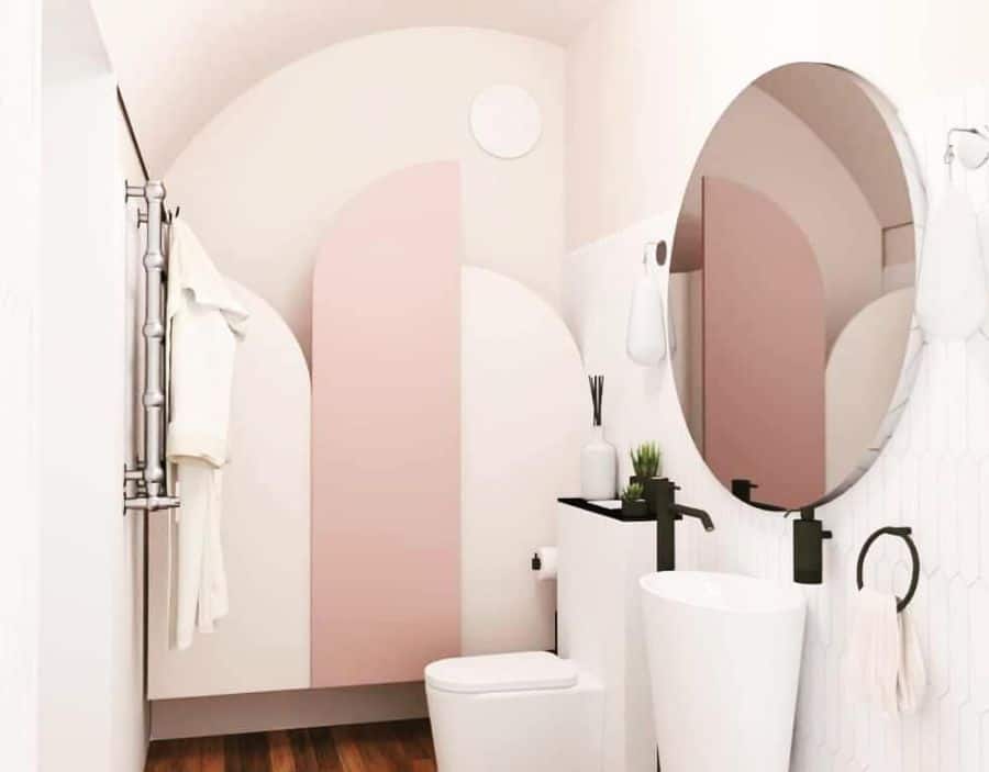 Small bathroom with pink and white curved wall design, round mirror, and towel on a ring holder.