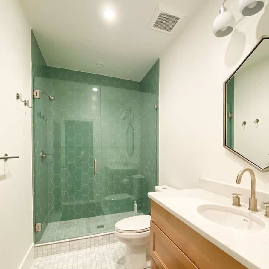 Bathroom with green hexagon-tiled shower, glass enclosure, and wooden vanity with sink.