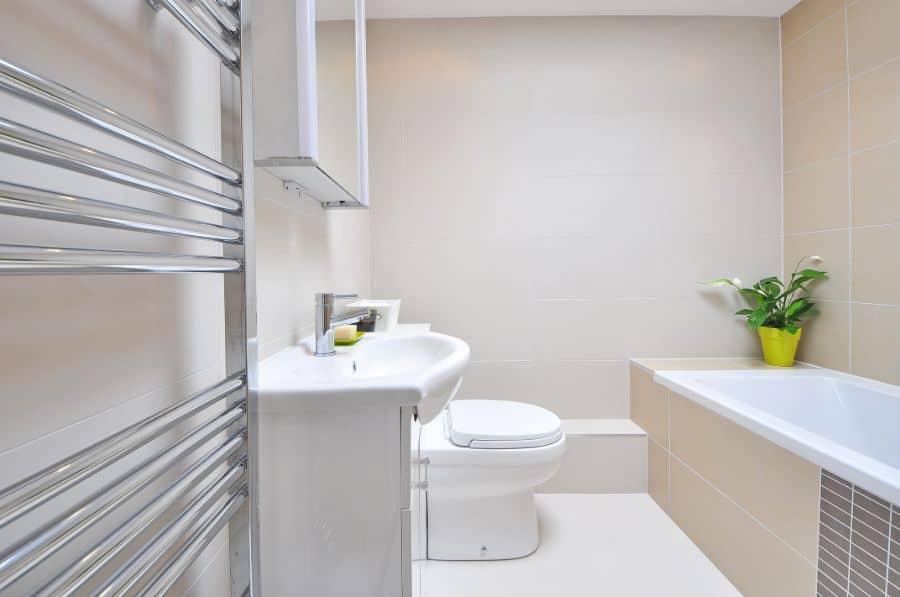 Modern beige bathroom with bathtub, sleek white sink, and a yellow potted plant.