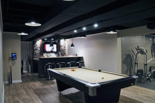 Modern mancave with pool table, sleek bar area, wood flooring, and adjacent fitness room.