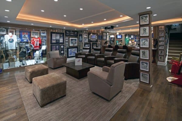 Luxury sports-themed mancave with leather recliners, framed memorabilia, display cases, and wood flooring.