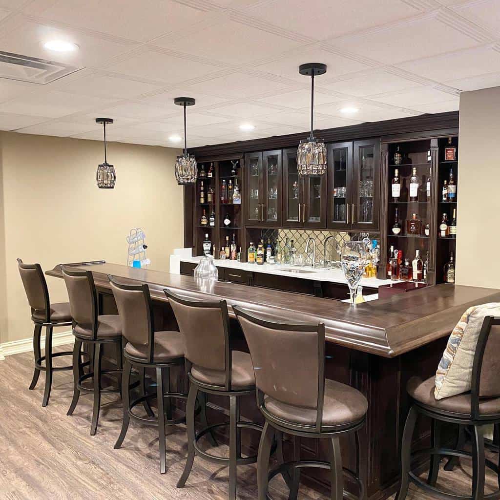 Traditional basement bar with dark wood cabinetry, leather stools, and pendant lighting.