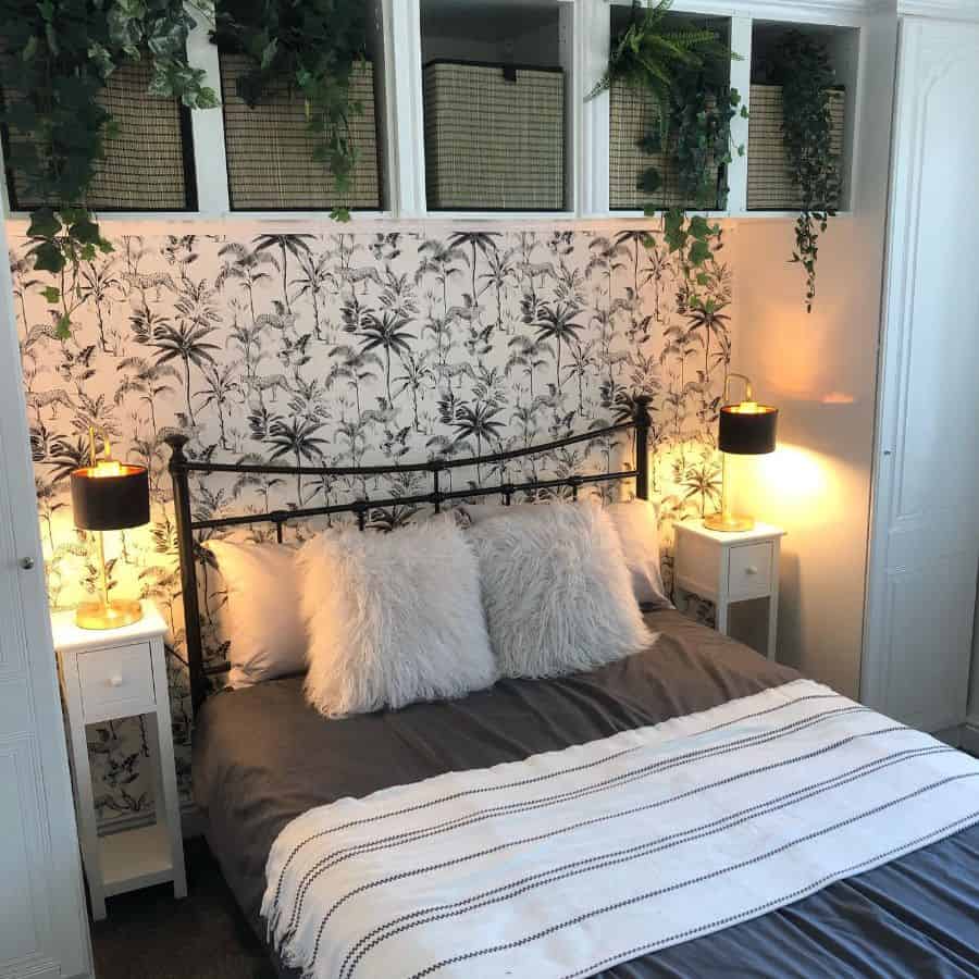 Bedroom with wicker basket storage above bed, botanical wallpaper, and two lamps.