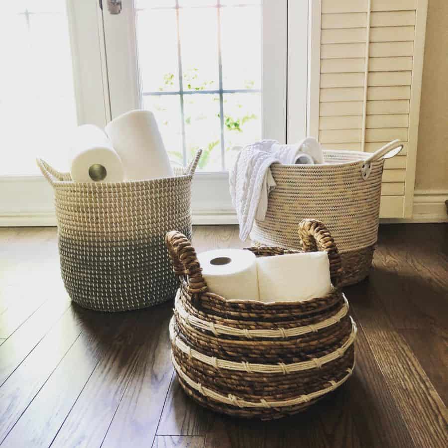 Three wicker baskets holding paper towels and towels, placed on a wooden floor near windows.