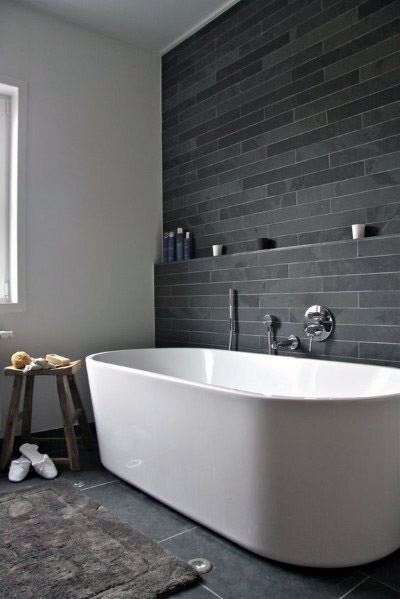 Modern bathroom with a white bathtub, grey tiled wall, and wooden stool