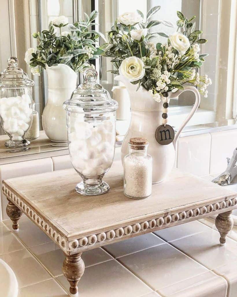 Decorative wooden tray with vases of flowers, cotton ball jars, and bath salts on a countertop.